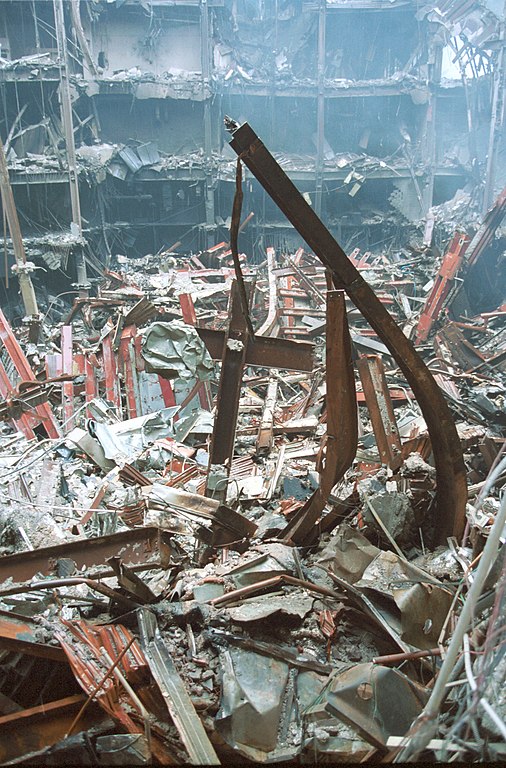 A photograph of the debris of the World Trade Center after the September 11 attacks in 2001. Among the ruins, two steel beams form a cross that would come to be known as the Ground Zero Cross.